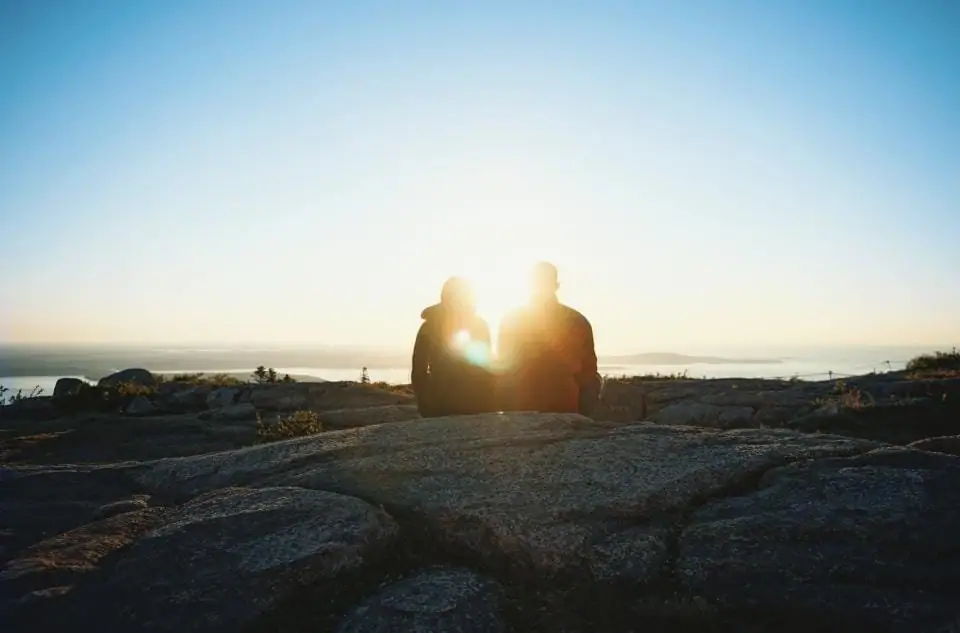 Casal observando o pôr do sol no mar