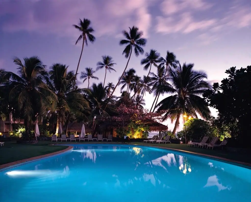 Piscina iluminada ao entardecer entre coqueiros